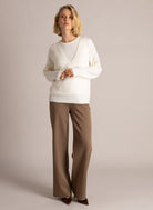 Full-length woman modelling an ivory V-neck layered sweater with long sleeves and brown wide-leg trousers, styled with brown pointed-toe heels.