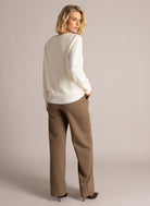 Back view of a woman wearing an ivory long-sleeve V-neck layered sweater with ribbed trim and brown wide-leg trousers.