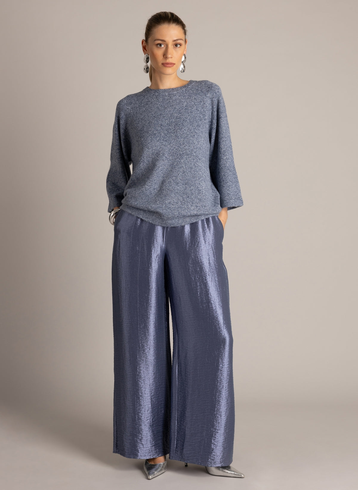  Model wearing a blue-grey textured knit top with three-quarter sleeves and wide-leg, metallic blue-grey trousers.