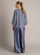 Model wearing a blue-grey textured knit top with three-quarter sleeves and wide-leg, metallic blue-grey trousers.
