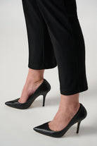 Black high-heeled shoes worn with black pants on a light gray background