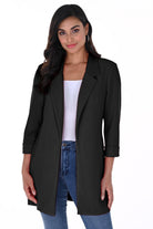Woman wearing a Black Cleo Longline Blazer with a relaxed open-front design, rolled cuff sleeves, and slim-fit jeans.