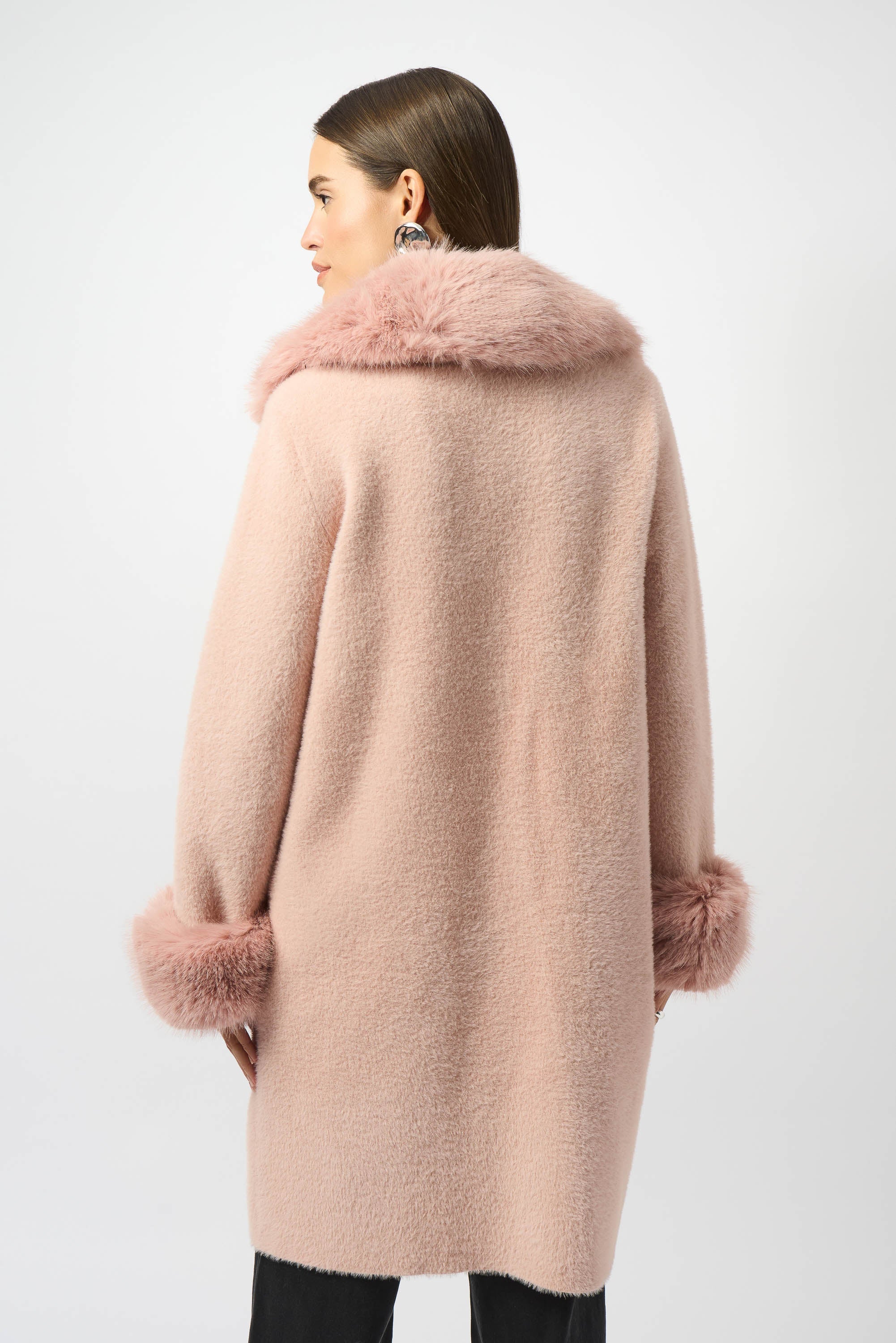 Woman wearing a pink coat with fur trim on a white background facing backwards