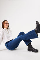 Women's dark blue bootcut jeans with a mid-rise fit, styled with a white button-down shirt and black ankle boots.