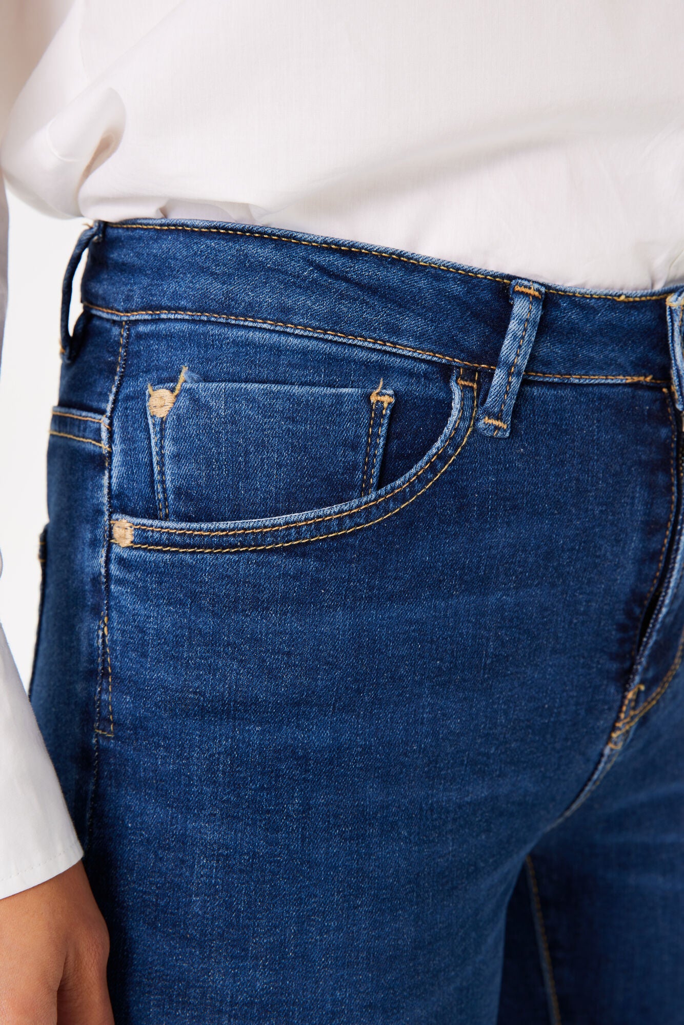 Close-up of women's dark blue denim bootcut jeans showing the front pocket, contrast stitching, and mid-rise waistband.