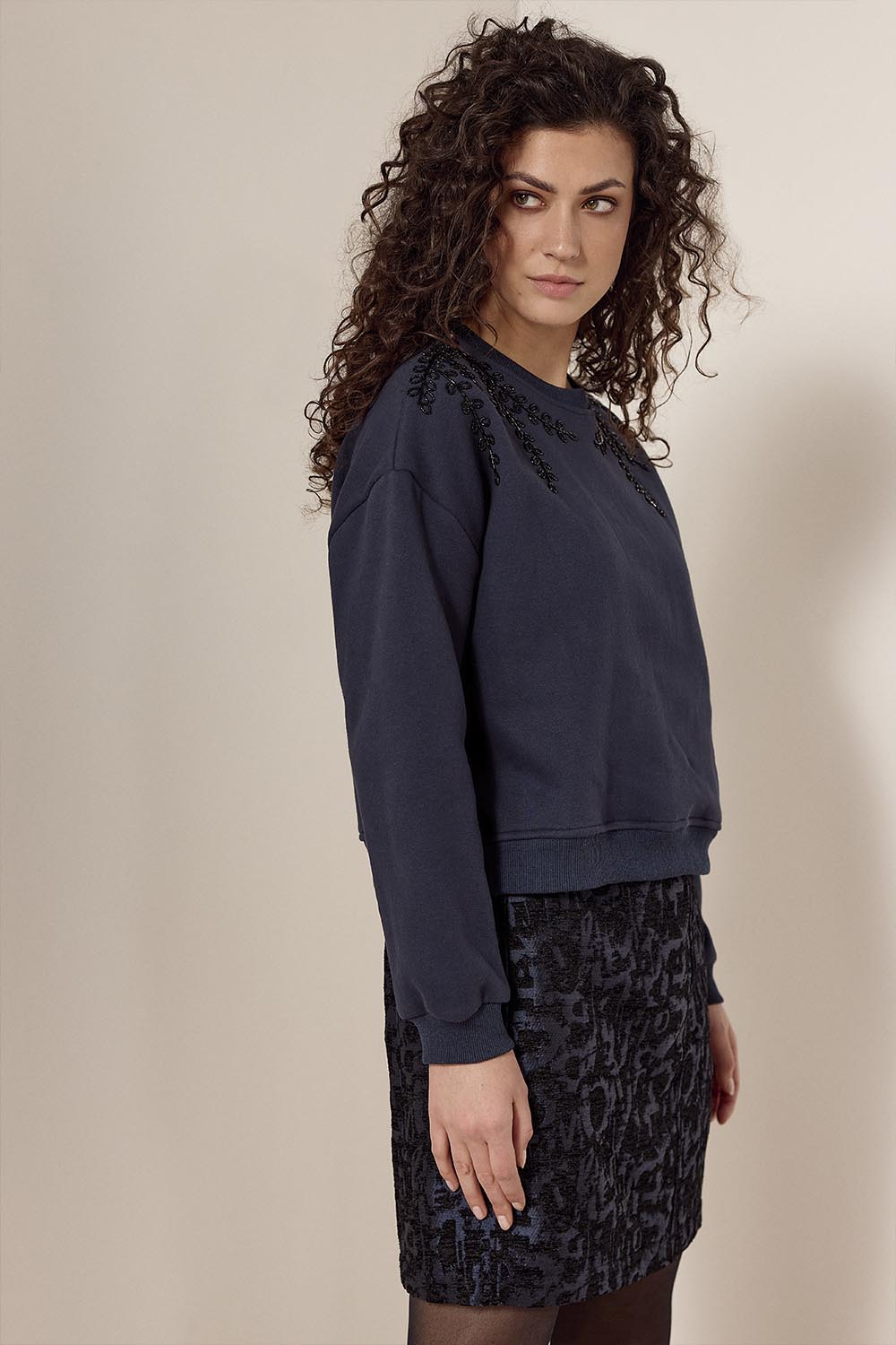 Woman wearing a navy blue sweatshirt and patterned skirt against a beige background