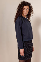 Woman wearing a navy blue sweatshirt and patterned skirt against a beige background
