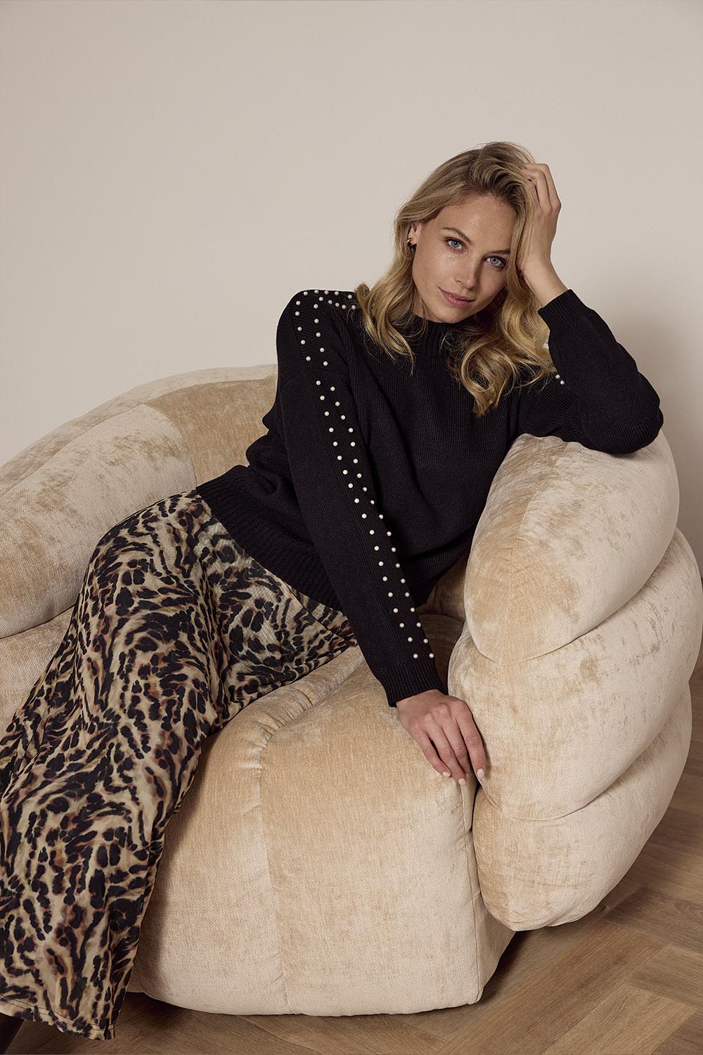 Woman in black top and leopard print pants sitting on a beige bean bag chair.