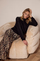 Woman in black top and leopard print pants sitting on a beige bean bag chair.
