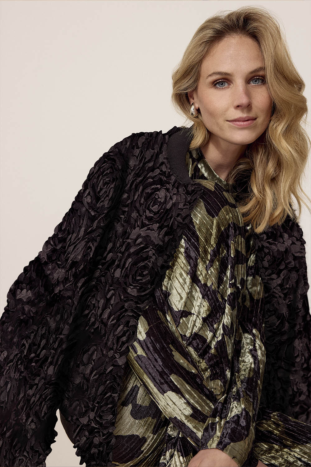 Woman wearing a dark floral jacket over a patterned dress on a plain background