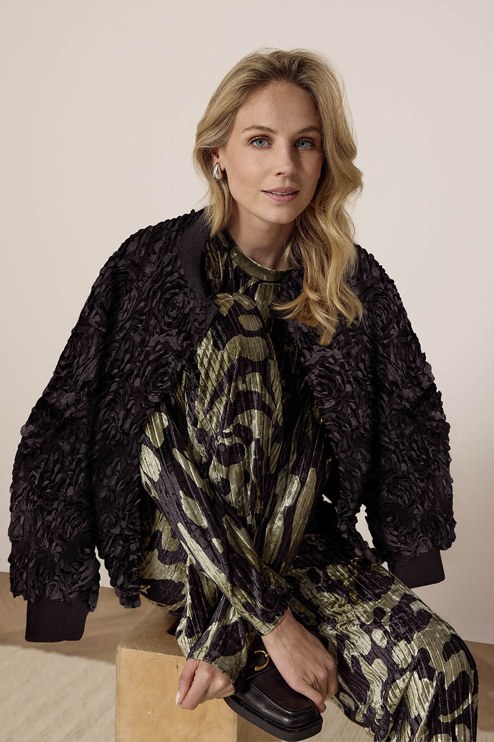 Woman wearing a black textured jacket over a patterned outfit on a beige background