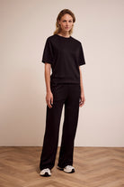 Woman wearing a black outfit standing on a wooden floor with a beige wall background