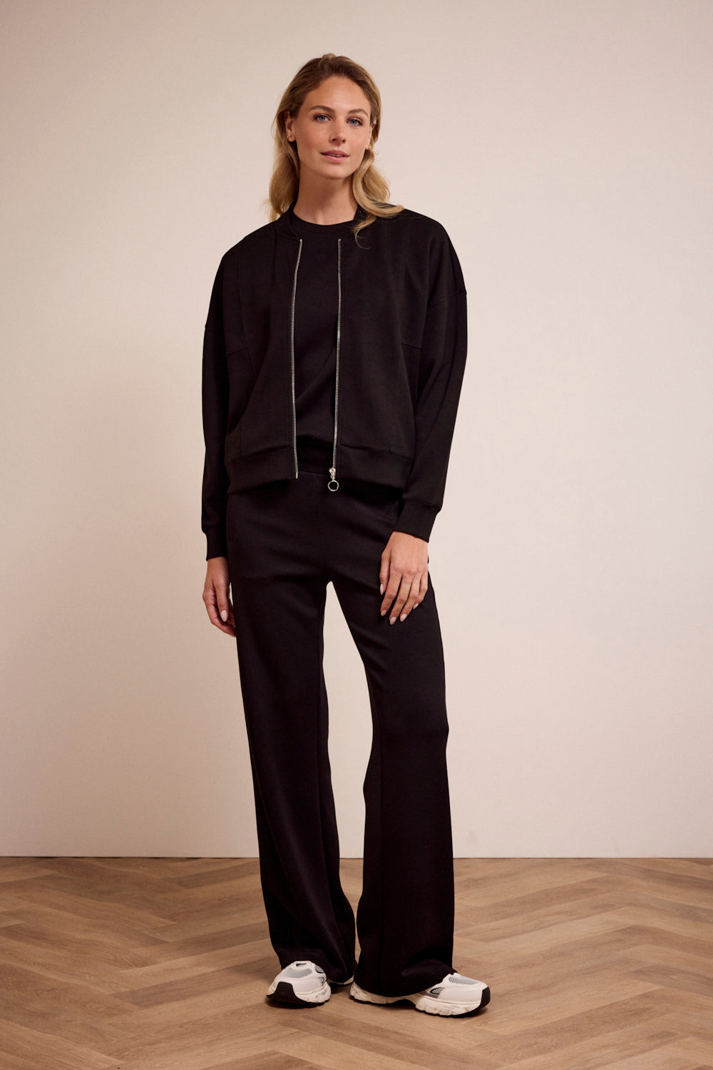 Woman wearing a black outfit with white sneakers on a beige background