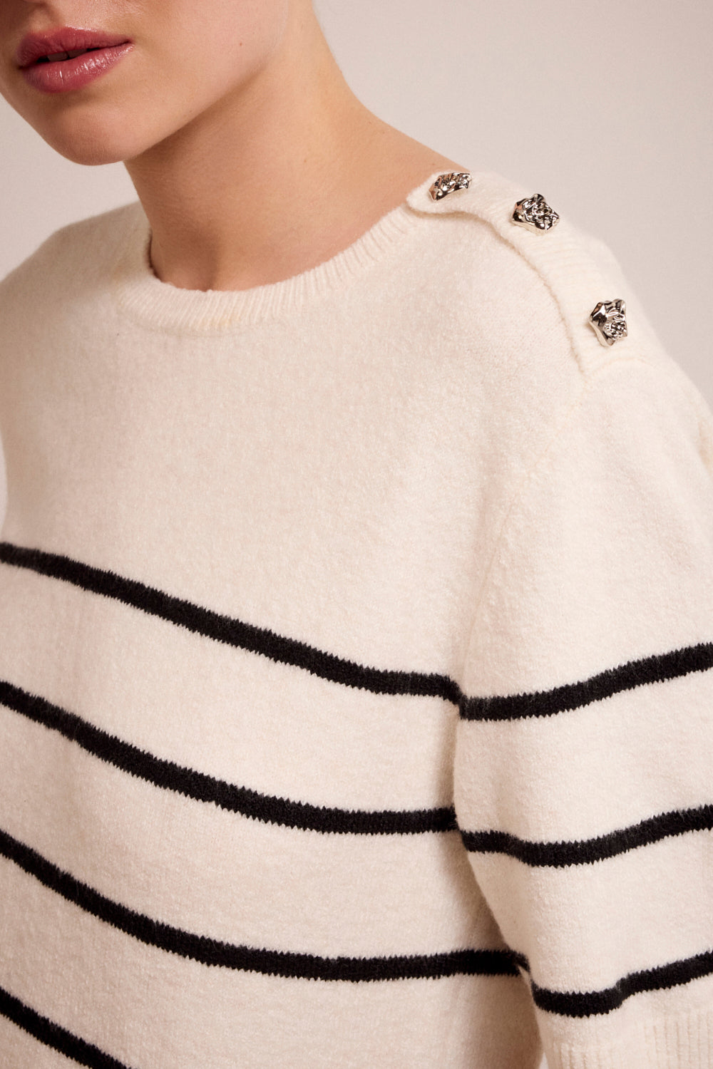 Close-up of a white sweater with black stripes and decorative buttons.