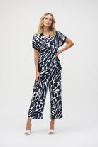 Woman in full-length view wearing the abstract print blouse with matching wide-leg pants and white heeled sandals.