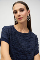 Close-up of woman wearing a navy textured top with short sleeves, showcasing the fabric detail and silver hoop earrings.