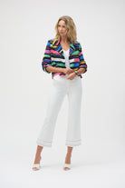 Woman posing in a studio wearing a colourful striped blazer and white cropped pants with fringe hem.