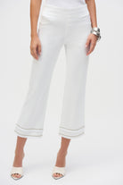Front view of white cropped pants showing the clean waistband and fringe hem, styled with a white tank and silver bangles.