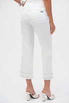 Back view of white cropped pants with patch pockets and fringe trim at the hem, worn with white heels.