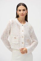Mid-shot of woman wearing cream open knit cardigan with gold-tone buttons and patch pocket details.