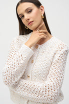 Close-up of woman wearing gold jewellery and textured cream cardigan with open knit pattern.