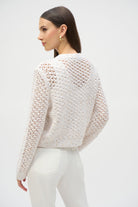Back view of woman wearing cream open stitch chenille cardigan styled with white pants.