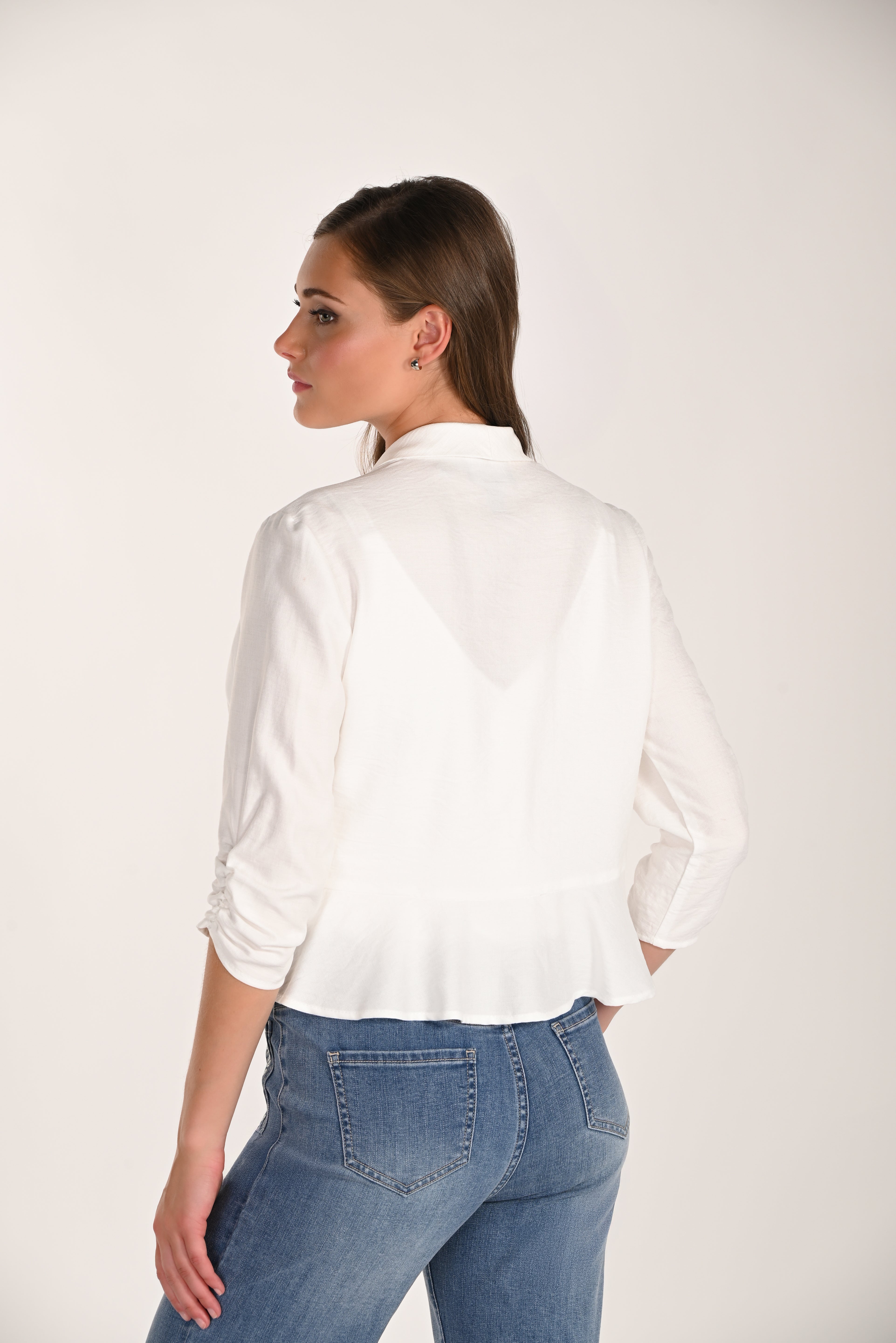 Back view of a women’s white drape jacket with ruched 3/4 sleeves paired with light wash jeans.