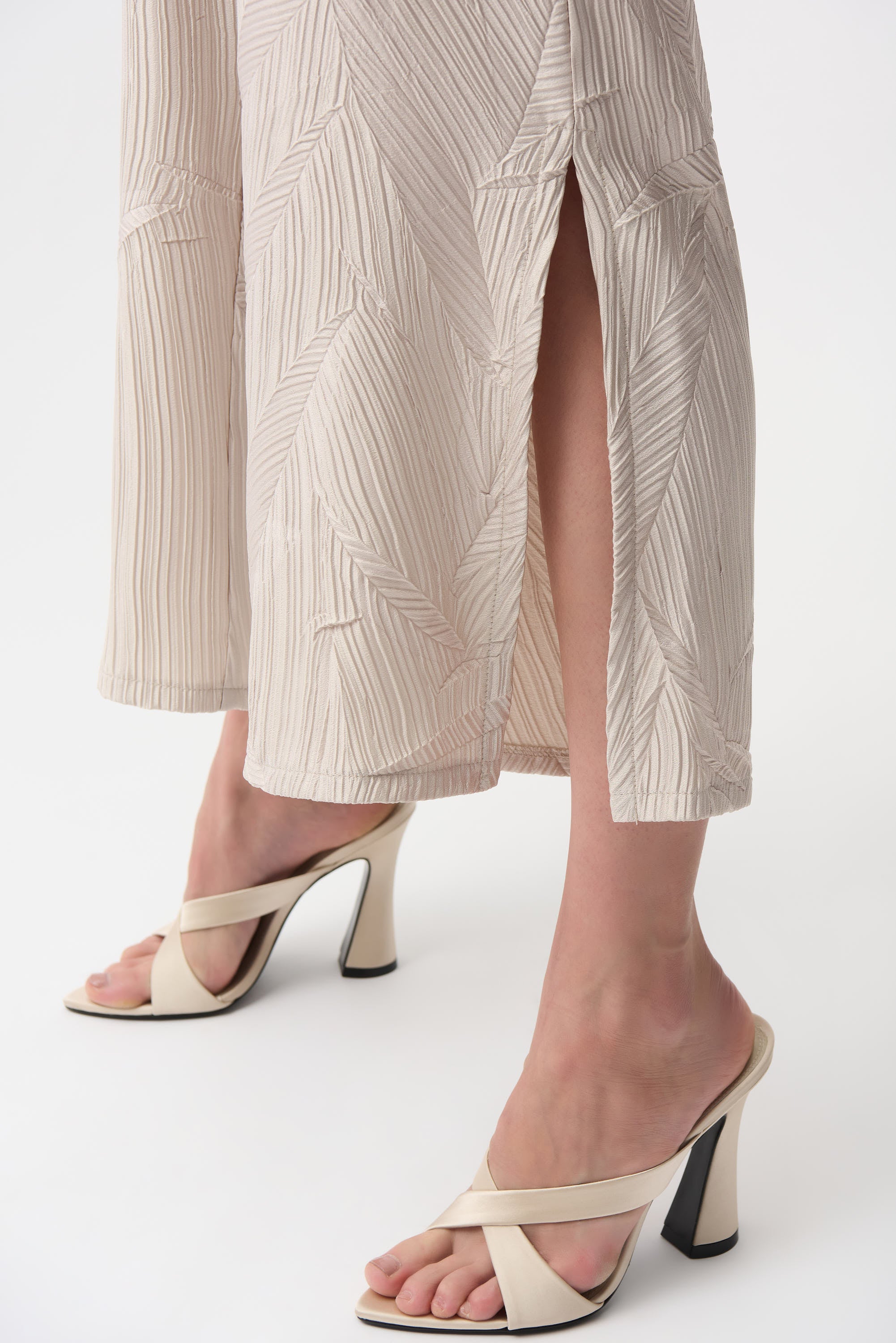 Close-up of legs in pleated satin pull-on culotte pants with side slits, paired with stylish high-heeled sandals.