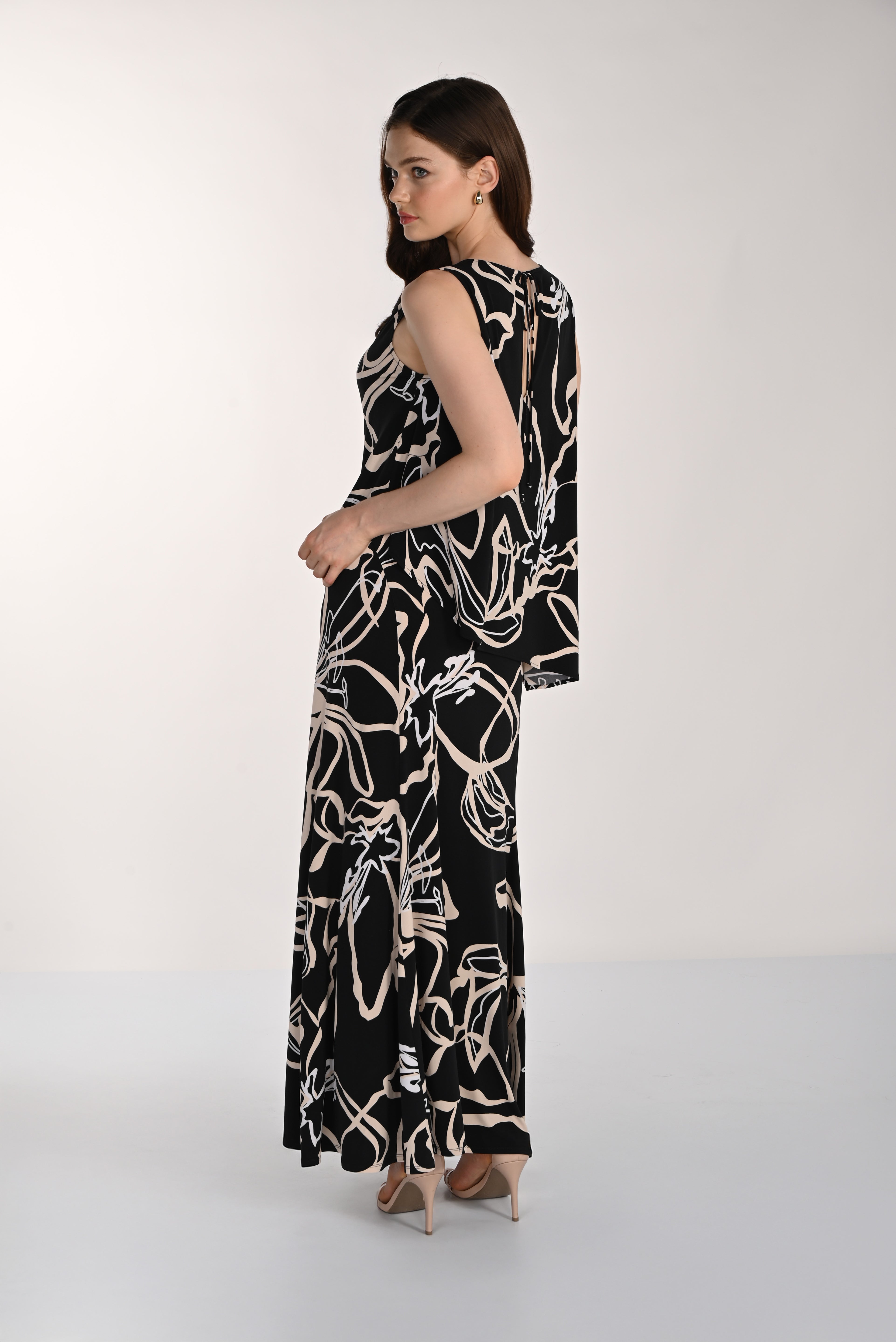 Side and back view of a women’s black sleeveless maxi dress with an abstract beige floral print, showcasing the layered overlay detail, relaxed drape, and back keyhole closure.