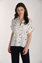 Front view of a model wearing the Wildflower Stitch Shirt, a relaxed button-front blouse with floral embroidery, rolled short sleeves, and a lightweight rayon-linen fabric blend.