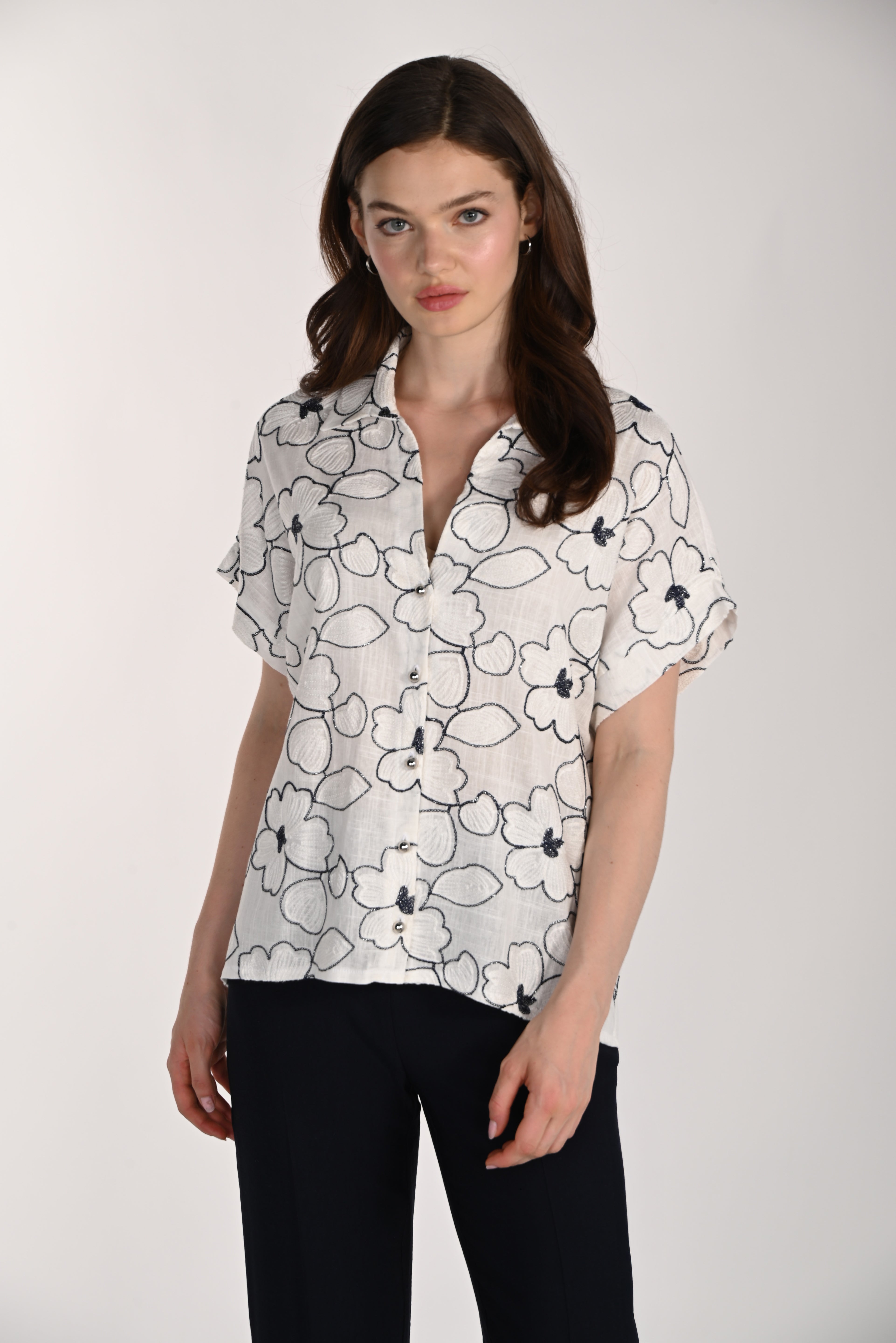 Front view of a model wearing the Wildflower Stitch Shirt, a relaxed button-front blouse with floral embroidery, rolled short sleeves, and a lightweight rayon-linen fabric blend.