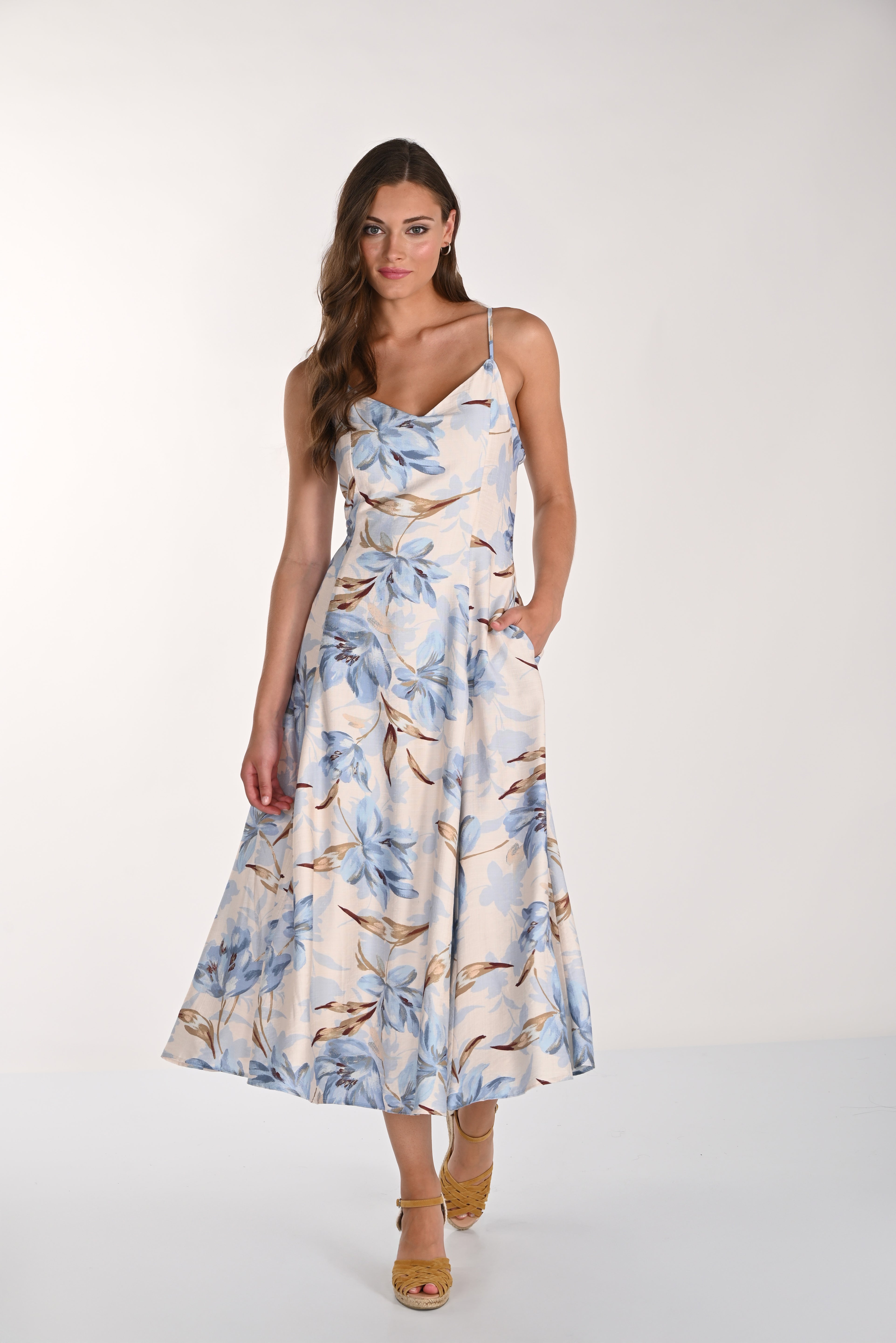 Women's blue floral midi slip dress featuring a soft cowl neckline, adjustable spaghetti straps, and a flowing A-line silhouette. Styled with wedge sandals and side pockets.