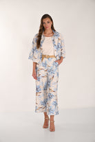 Women's blue floral wide-leg cropped pants styled with a cream sleeveless top, matching floral jacket, woven belt, and gold heeled sandals. Front full-length view.