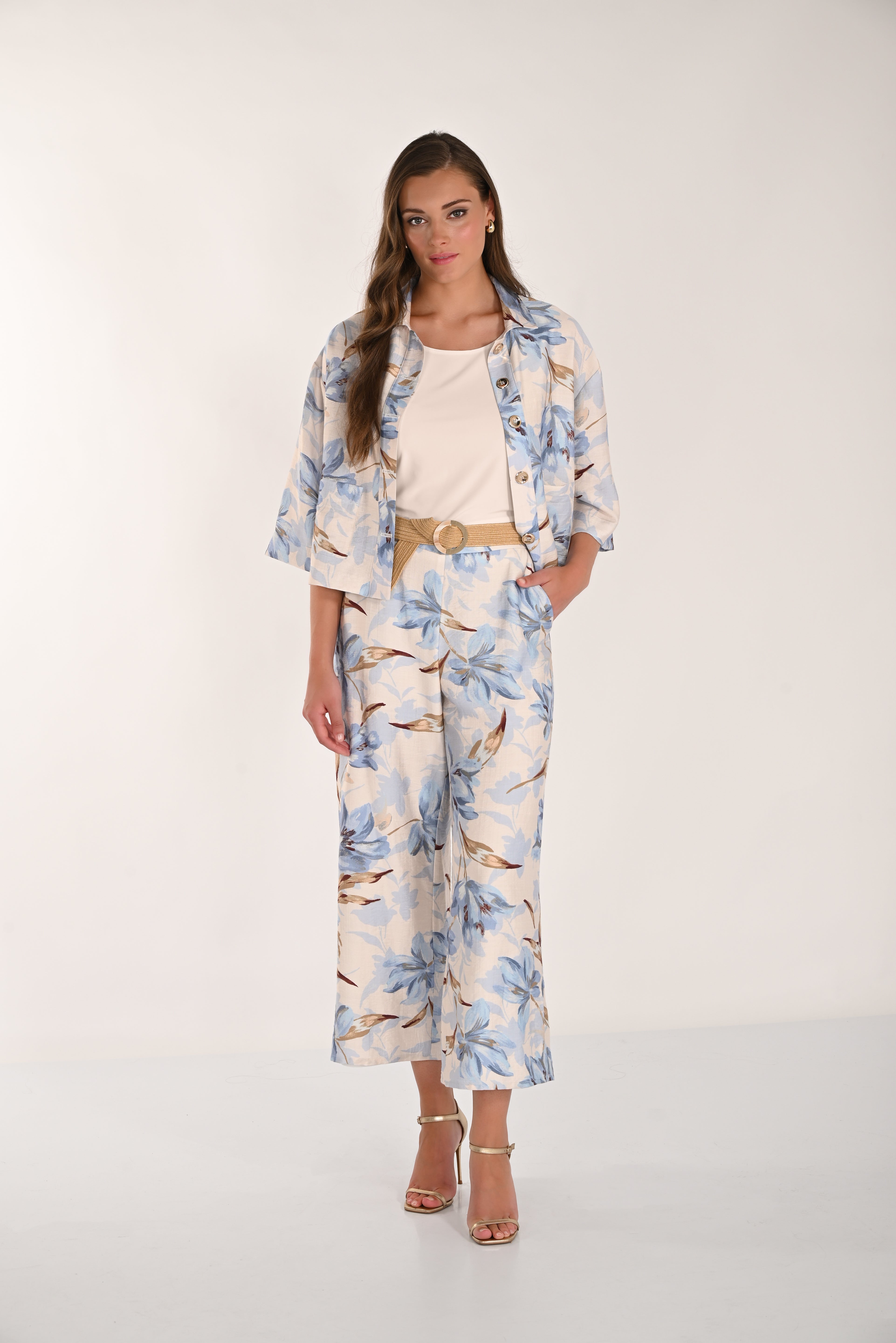 Women's blue floral wide-leg cropped pants styled with a cream sleeveless top, matching floral jacket, woven belt, and gold heeled sandals. Front full-length view.