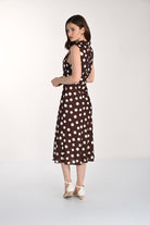 Women's sleeveless polka dot midi dress with a tie-neck detail, fitted waist, and flowing skirt. Shown from the back and side to highlight the silhouette and drape.