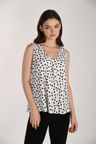 Model wearing a black and white polka dot sleeveless swing top featuring a V-neckline and flowing swing silhouette, paired with black fitted pants.