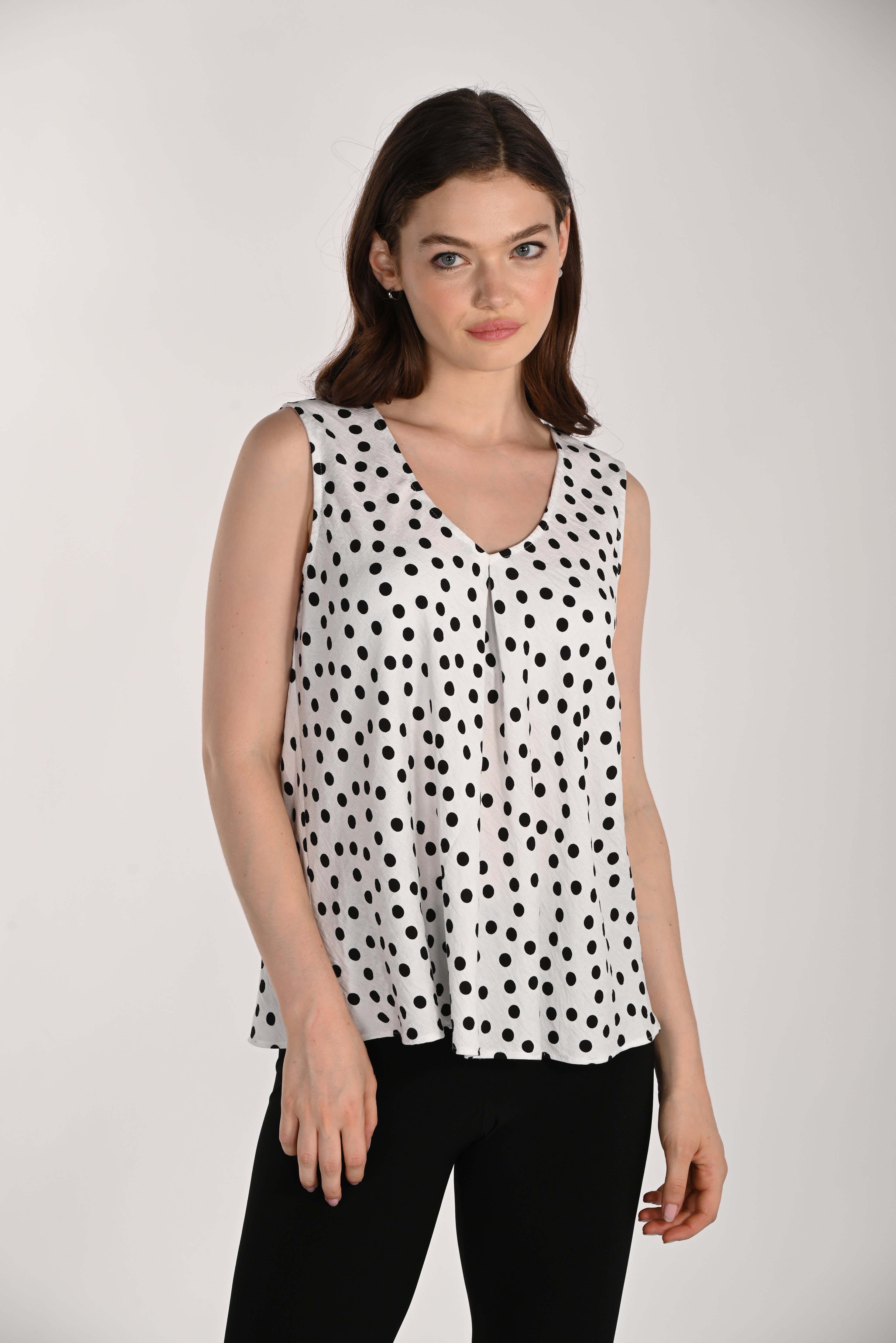 Model wearing a black and white polka dot sleeveless swing top featuring a V-neckline and flowing swing silhouette, paired with black fitted pants.