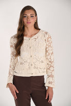 Model wearing a cream crochet cardigan featuring floral crochet detailing, button-front closure, long sleeves, and front patch pockets paired with brown trousers.