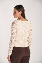Model wearing a cream crochet cardigan with intricate floral openwork detailing, long sleeves, and a lightweight cotton knit design shown from the back.