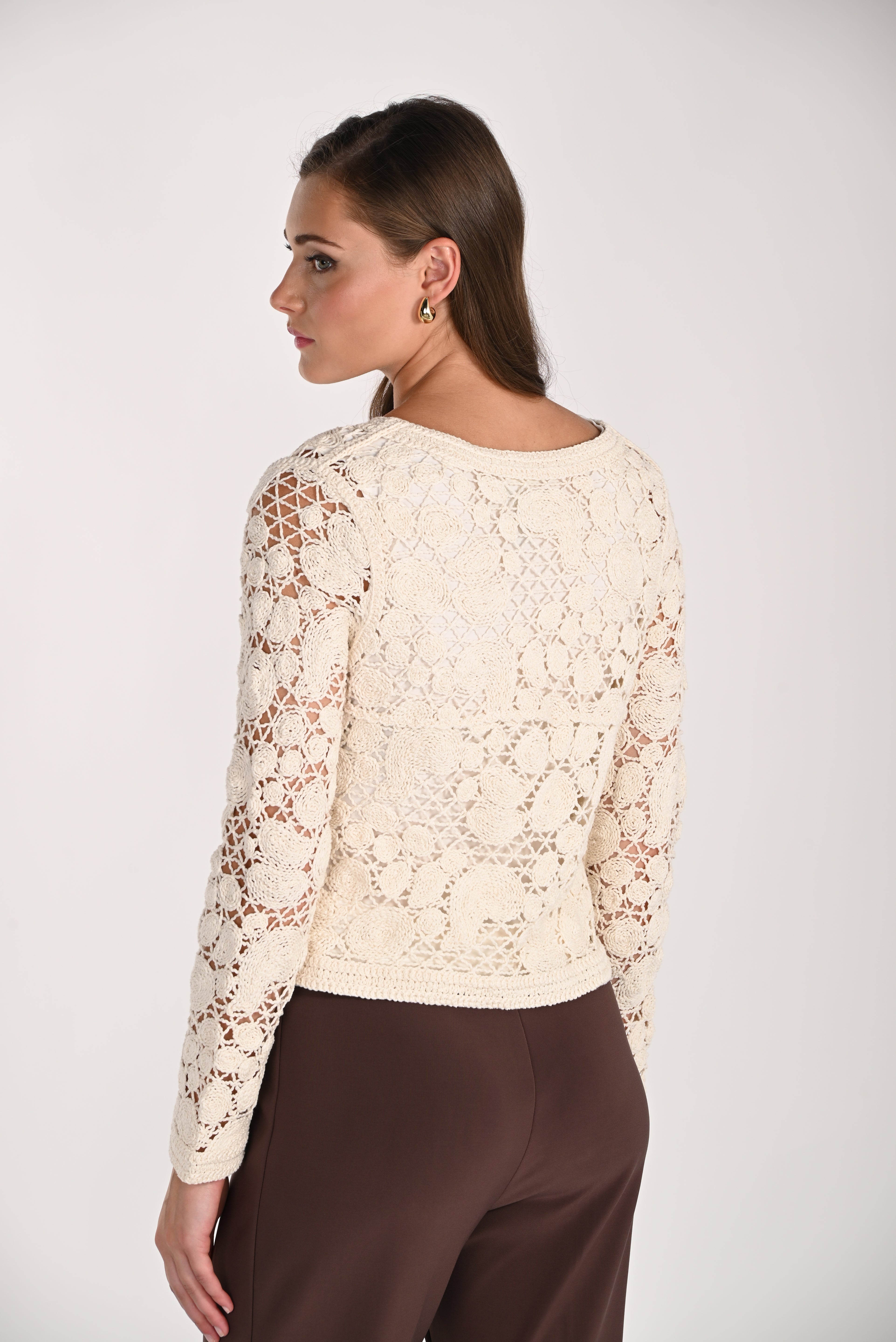 Model wearing a cream crochet cardigan with intricate floral openwork detailing, long sleeves, and a lightweight cotton knit design shown from the back.