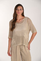 Woman modelling a beige metallic open-knit top with a relaxed fit, round neckline, and elbow-length sleeves. The lightweight mesh-knit texture features a subtle shimmer and is paired with loose, crinkled wide-leg trousers.