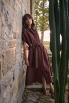 Woman in a brown dress standing against a stone wall with cacti.