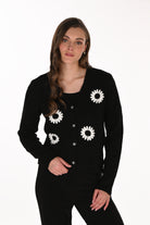 Women's button-front knit cardigan featuring oversized daisy appliqué details on the front. Designed with a relaxed fit, long sleeves, a round neckline, and decorative statement buttons. Styled with a coordinating top and fitted pants.