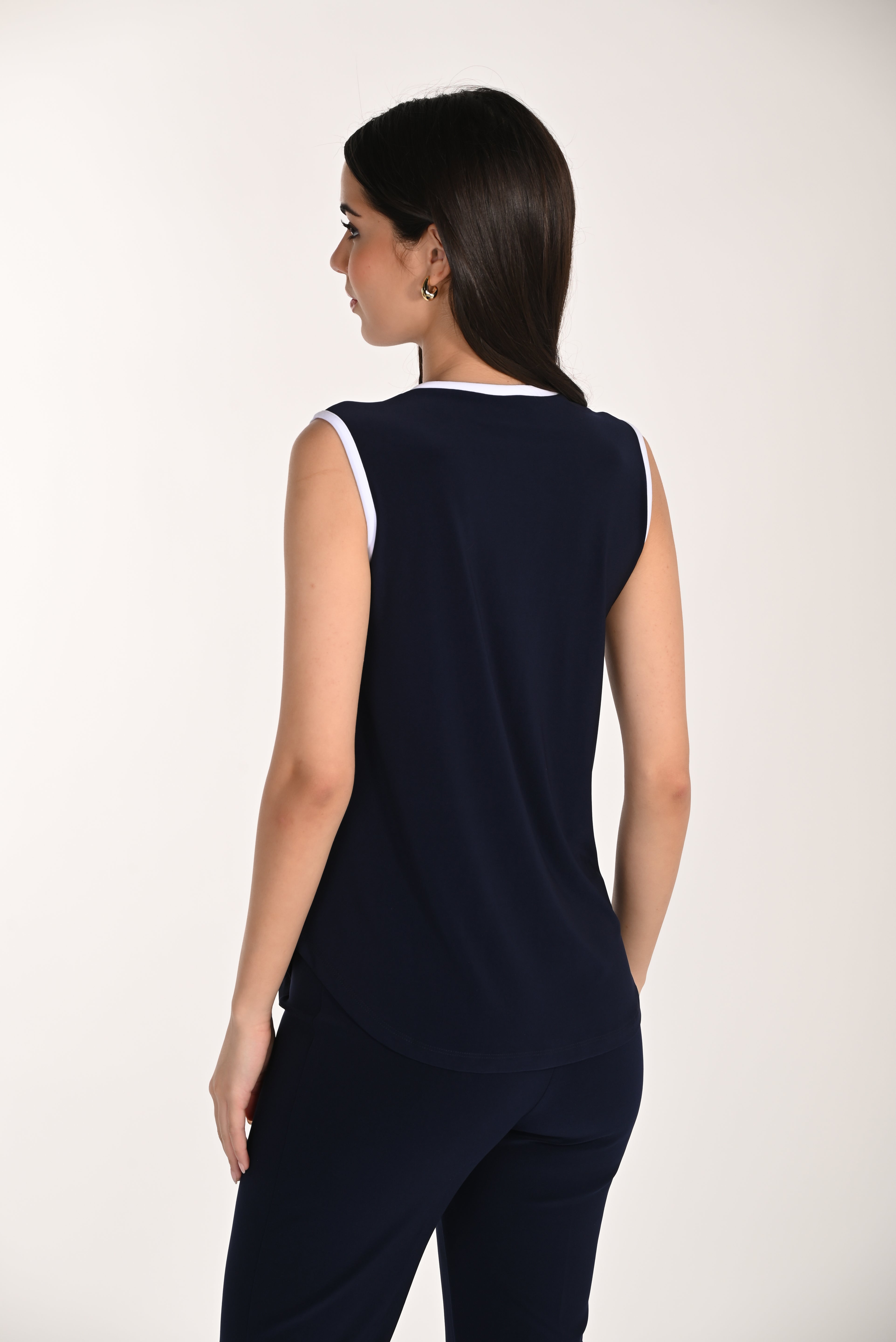 Back view of a women’s sleeveless navy knit top with white trim, featuring a relaxed fit and smooth drape paired with matching navy pants.