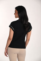 Woman wearing a black textured knit top with contrast trim detailing on the neckline and cap sleeves, shown from the back with beige fitted pants.