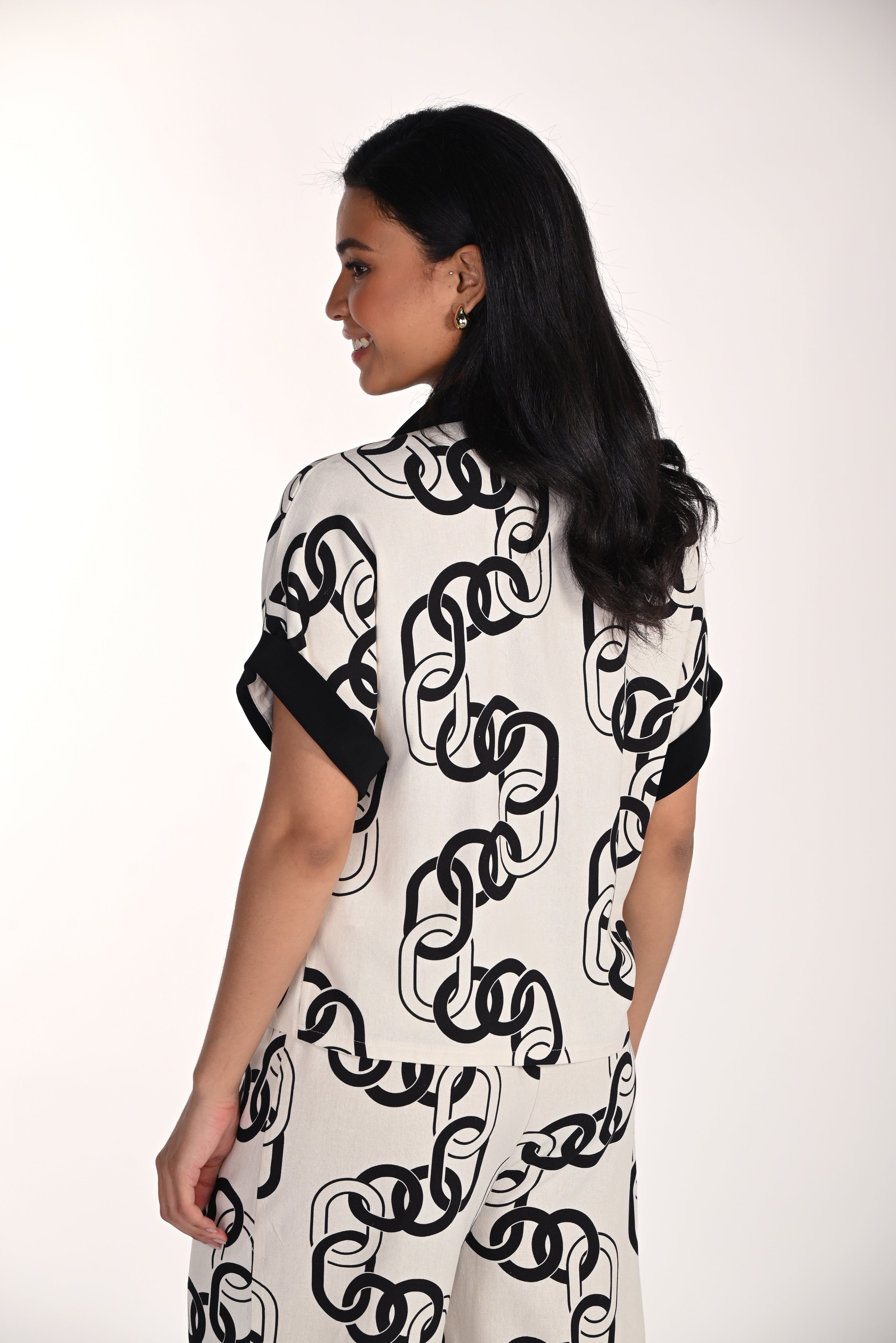 Back view of a woman wearing a relaxed chain print blouse with cuffed short sleeves and a soft, breathable drape. The all-over chain-inspired pattern and easy silhouette create a polished yet comfortable look.