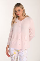Woman wearing a blush pink textured knit jacket with floral appliqué detailing, crystal-style buttons, long sleeves, and a round neckline, paired with floral print trousers.