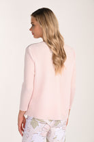 Back view of a blush pink textured knit jacket with a clean straight silhouette, long sleeves, and subtle ribbed texture, paired with floral print trousers.
