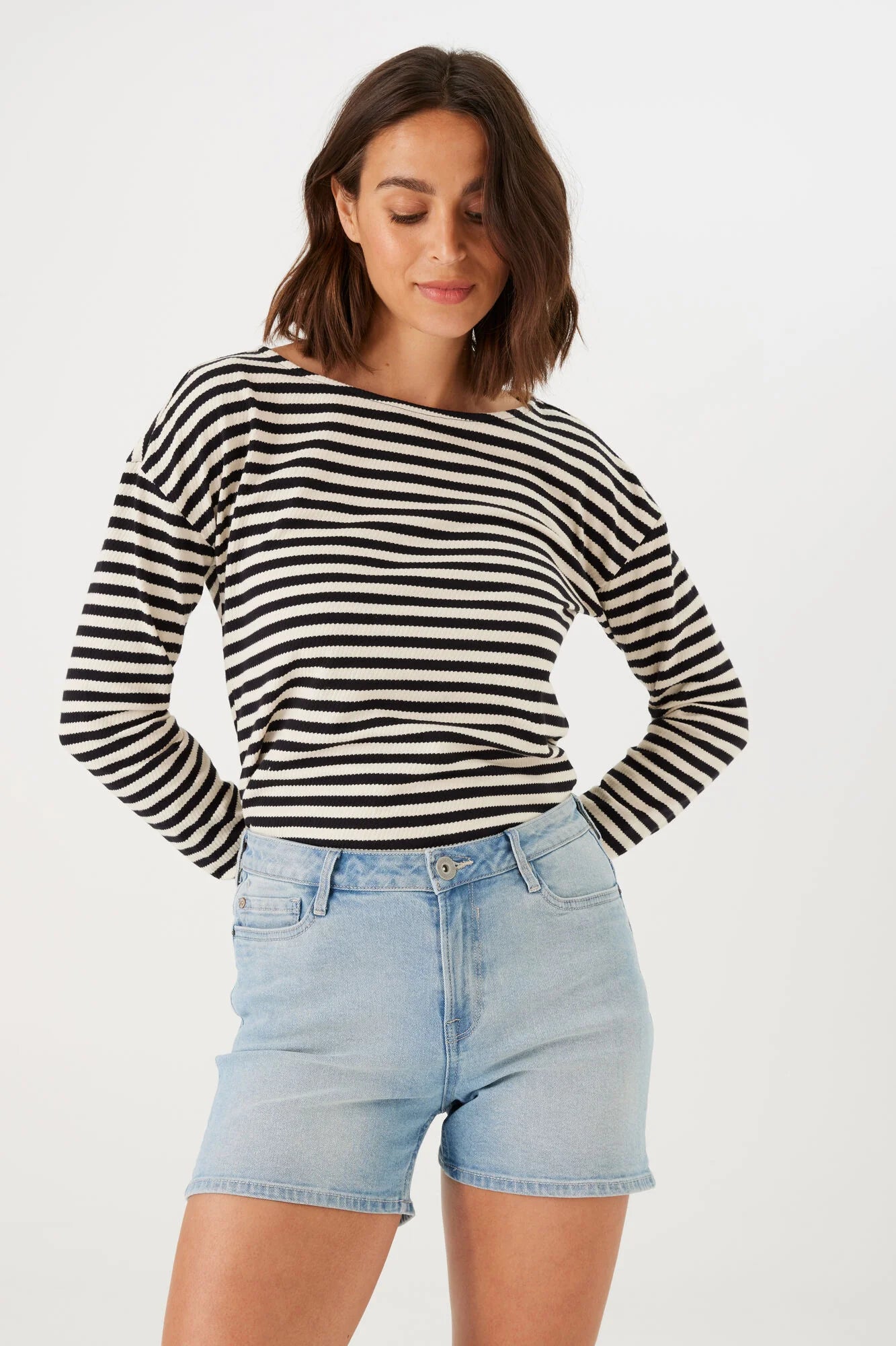 model wearing slim-fit Bermuda shorts with a mid-rise waist, styled with a long-sleeve striped top and flat sandals.