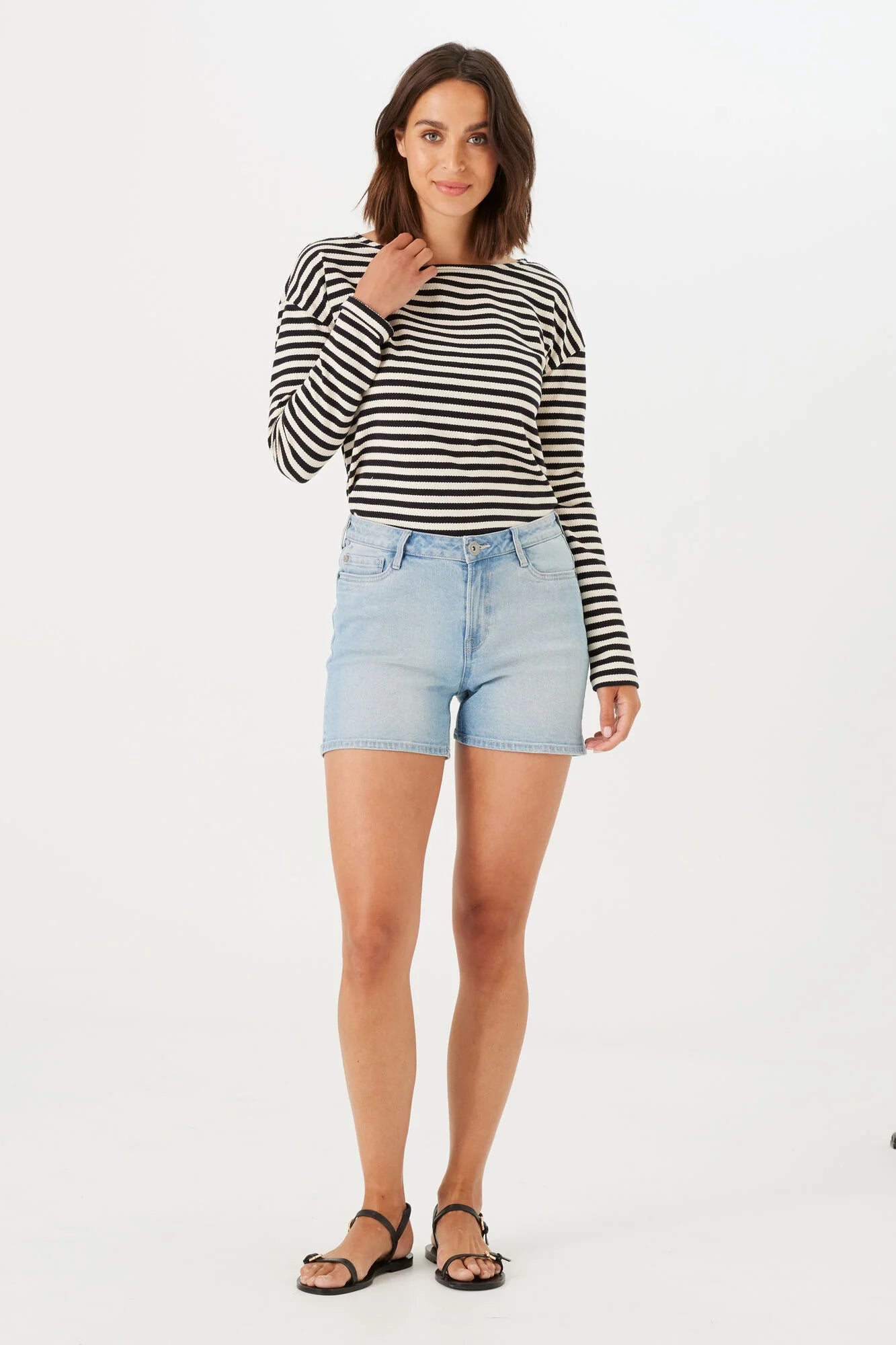 model wearing slim-fit Bermuda shorts with a mid-rise waist, styled with a long-sleeve striped top and flat sandals.